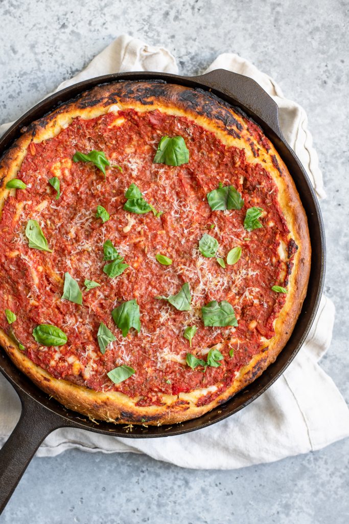 Chicago-style deep dish pizza baked in a cast iron skillet with fresh basil garnish